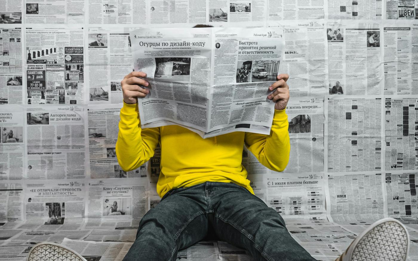 a person sitting on the floor reading a newspaper by Egor Vikhrev courtesy of Unsplash.