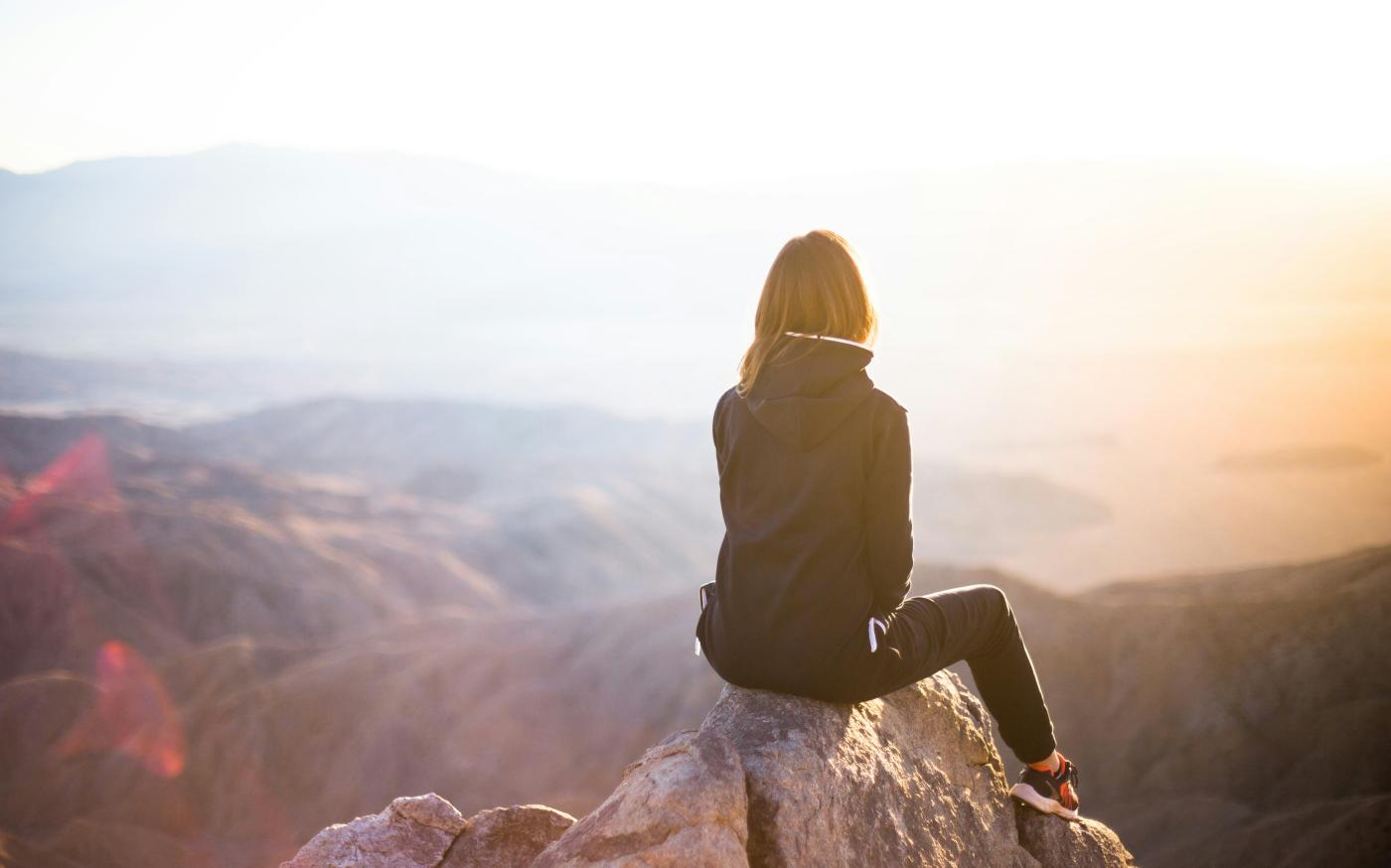 person sitting on top of gray rock overlooking mountain during daytime by Denys Nevozhai courtesy of Unsplash.