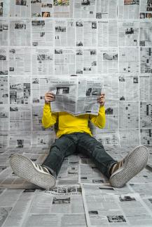 a person sitting on the floor reading a newspaper by Egor Vikhrev courtesy of Unsplash.