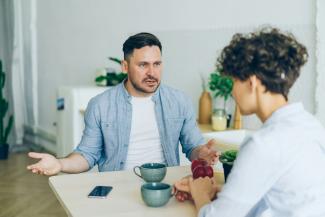 a man sitting at a table talking to a woman by Vitaly Gariev courtesy of Unsplash.