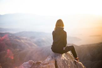 person sitting on top of gray rock overlooking mountain during daytime by Denys Nevozhai courtesy of Unsplash.