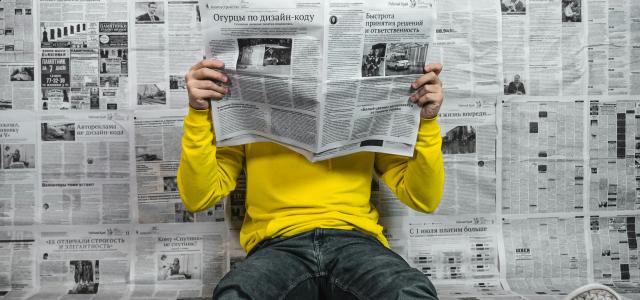 a person sitting on the floor reading a newspaper by Egor Vikhrev courtesy of Unsplash.