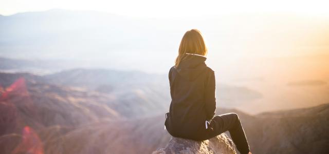 person sitting on top of gray rock overlooking mountain during daytime by Denys Nevozhai courtesy of Unsplash.